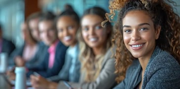 Smiling woman with curly hair in a professional setting, sitting with a diverse group of colleagues.