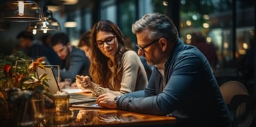 a person and person sitting at a table looking at a laptop