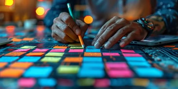 Hands organizing colorful sticky notes on a table with a laptop, in a warmly lit environment.